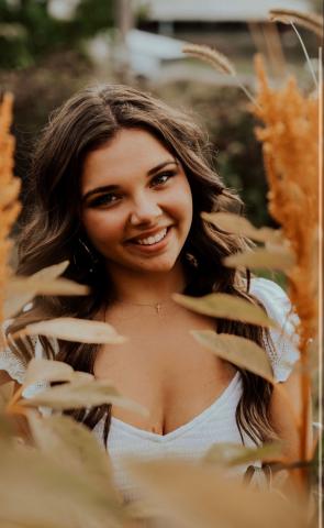 Corn and wheat surrounds Bryn Lahew's face as she smiles brightly at the camera.