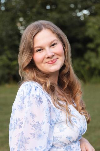 Lucia Lundgren smiles joyfully into the camera wearing a light shirt with blue flower patterns across it.