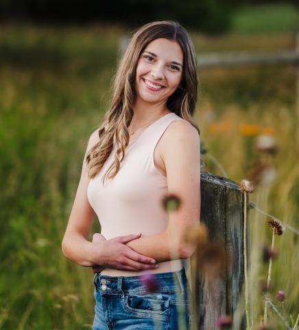 Madison Zeroski poses alongside a wooden fence amidst a field of flowers.