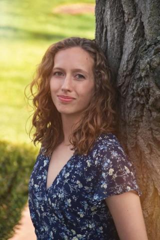 Lauryn is pictured in a blue and white dress as she leans against a tree.