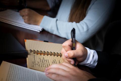 Student hand writing notes in a bound notebook