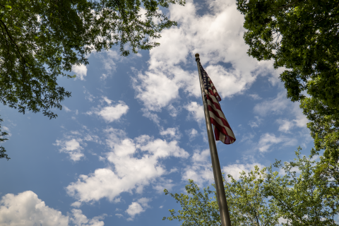 An American flag against the backdrop of a blue sky with scattered white clouds; taken in Veterans Memorial Plaza on Waynesburg's campus