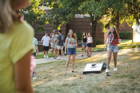 Two students smiling while playing cornhole, with other students in the background and foreground looking on