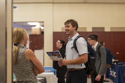 A student smiling while talking with an employer at the Business & Communication Job & Internship Fair in the Marsh Center