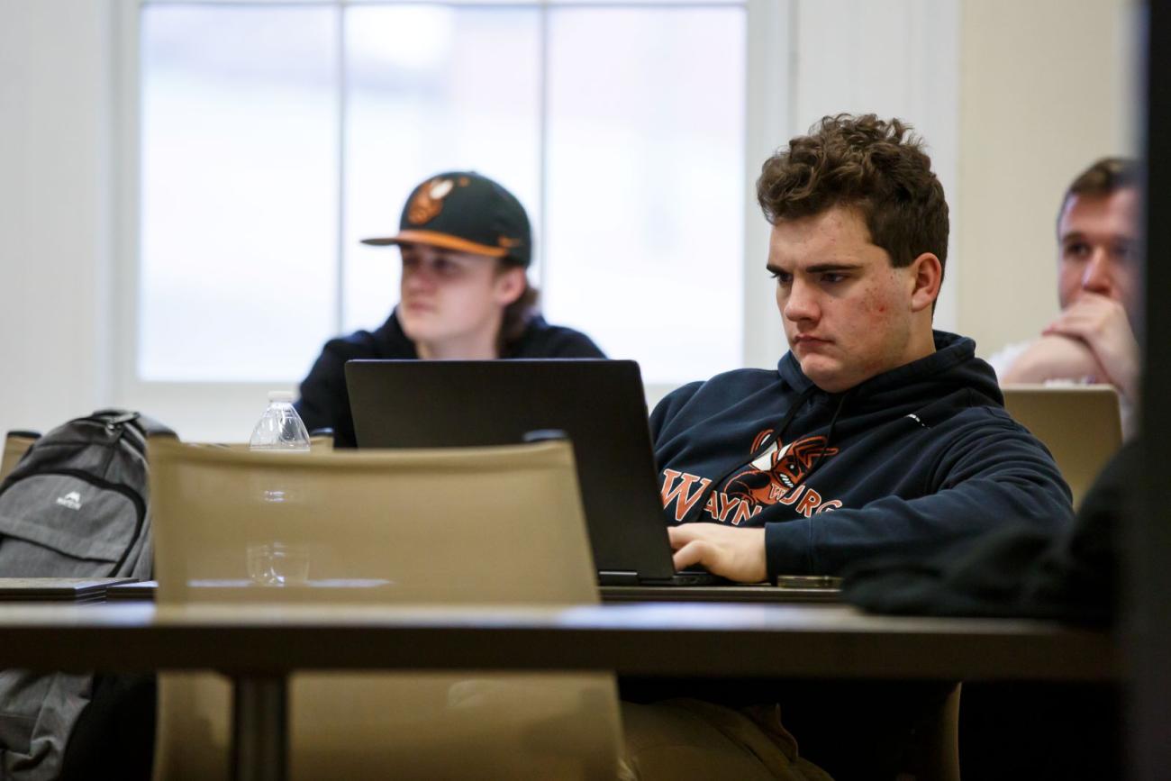 Waynesburg students listen to lecture in class with their laptops open.