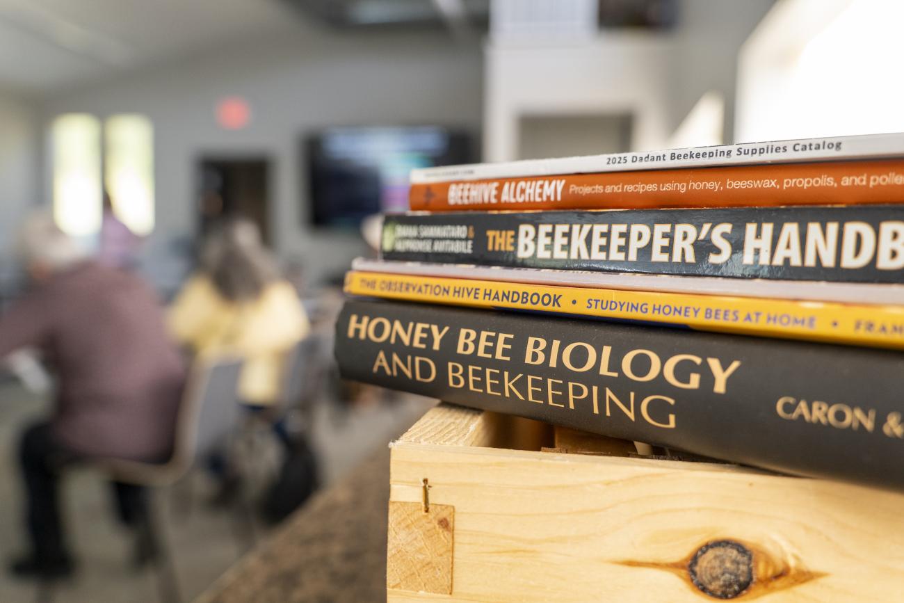 Beekeeping books stacked on a table with students in the background.