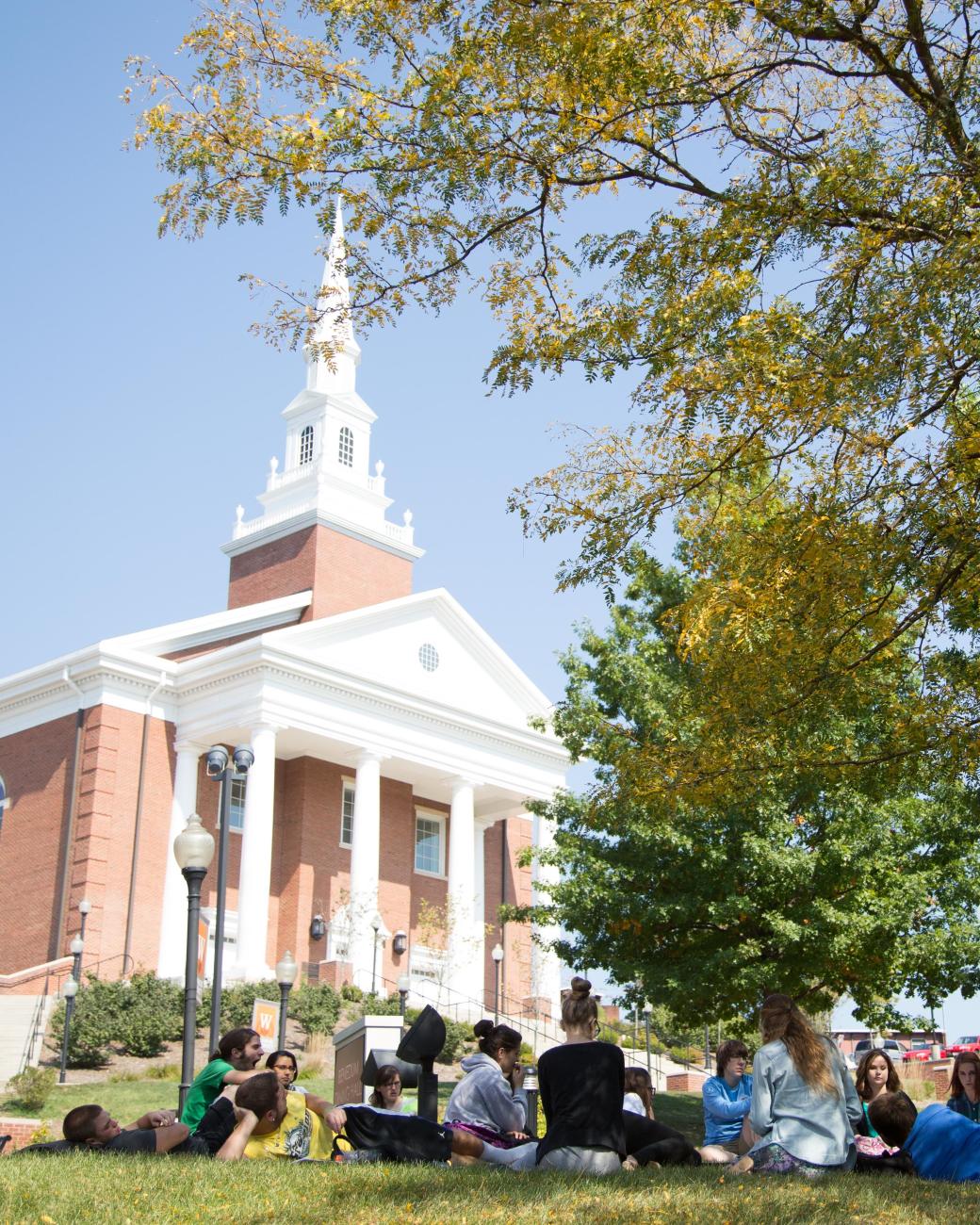 A group of students sit on the lawn in front of the Chapel.