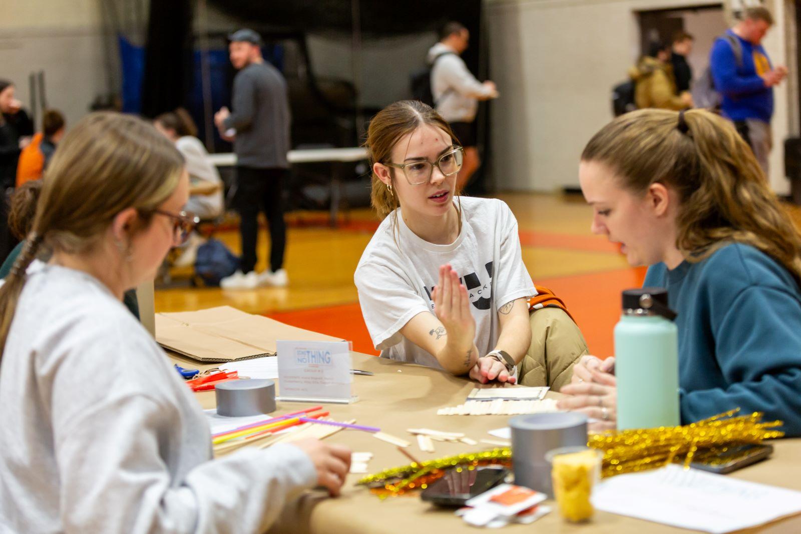 A student holds her arm out as she and another student discuss the project.