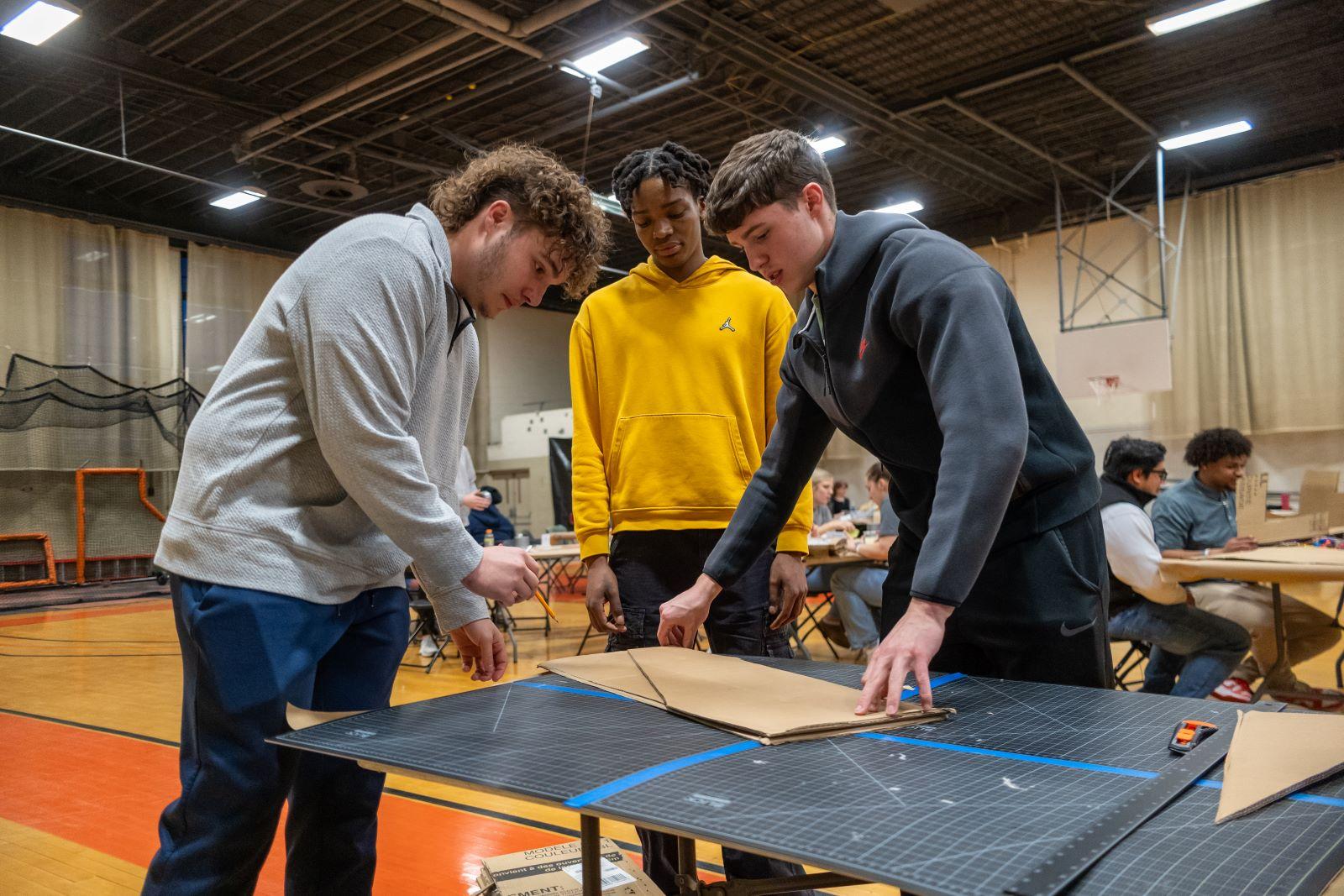 Three students work together to measure and cut a piece of cardboard