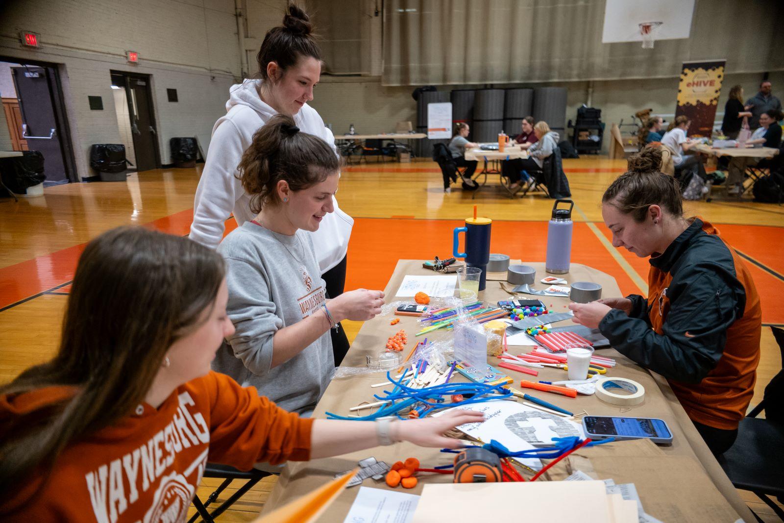A group of four girls laugh and talk as they work on their creative project