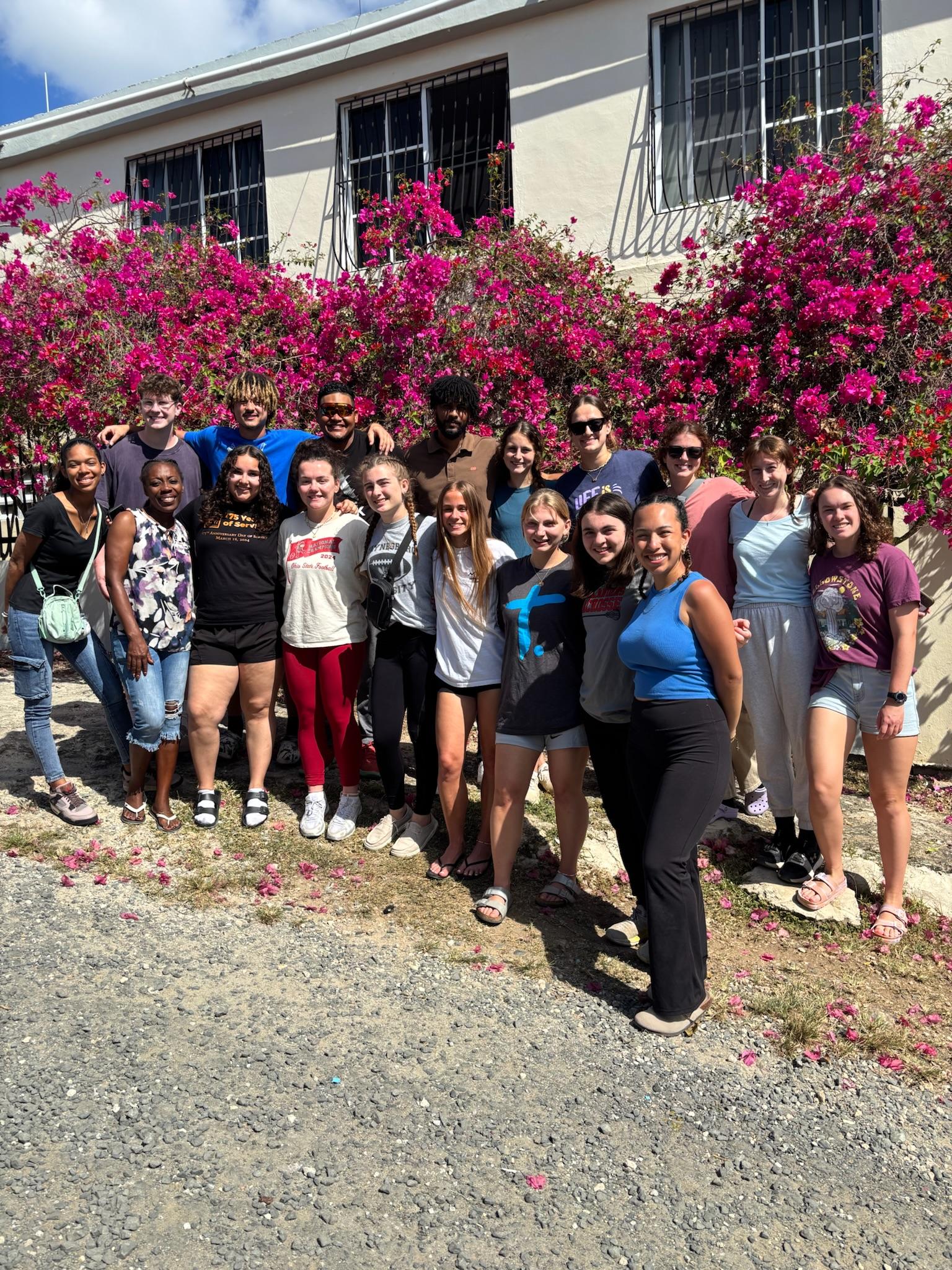 Project GROW group members stand in front of the blooming pink trees that outline the compound.
