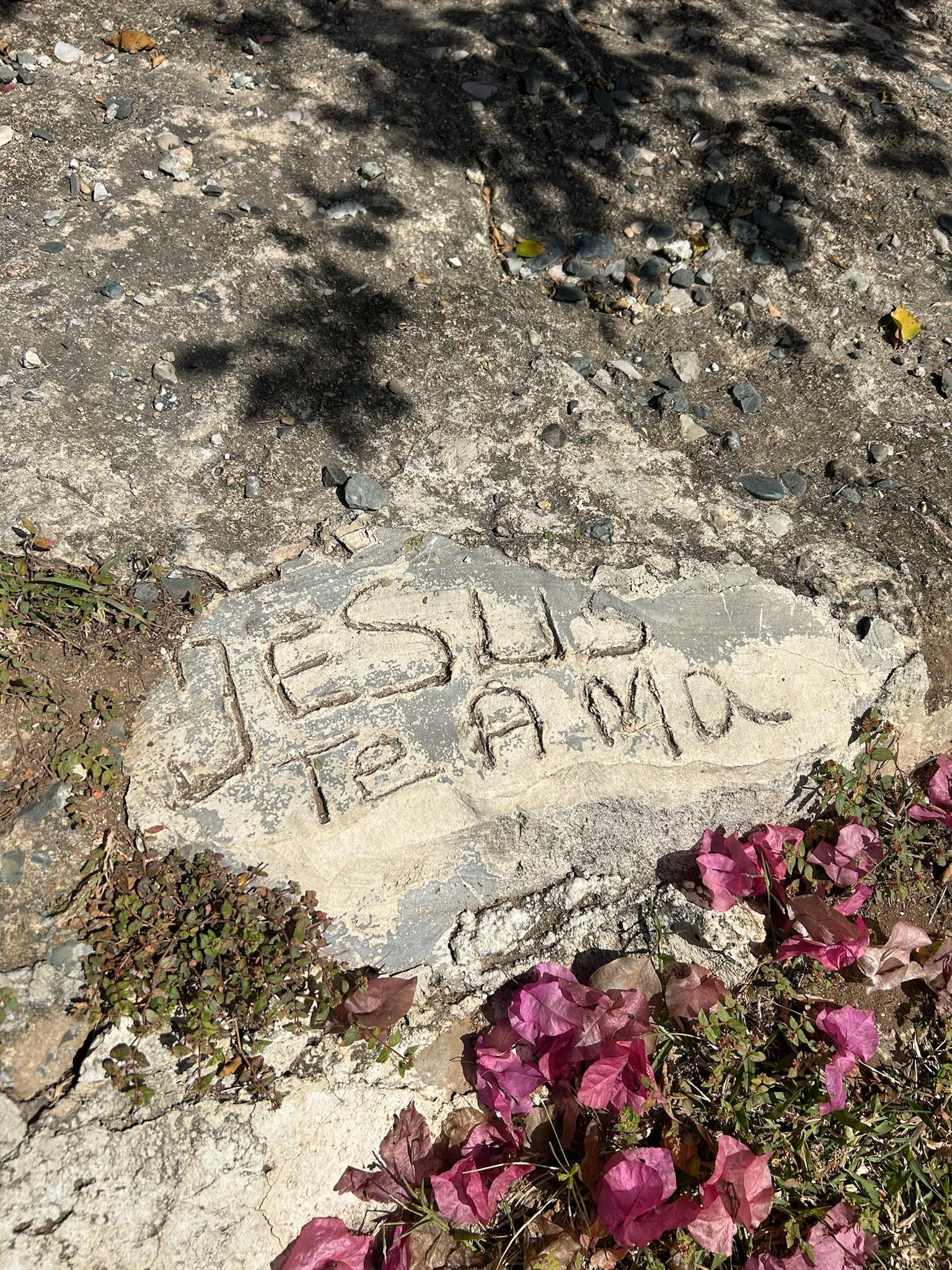A rock depicts "JESUS TE AMA" on its surface