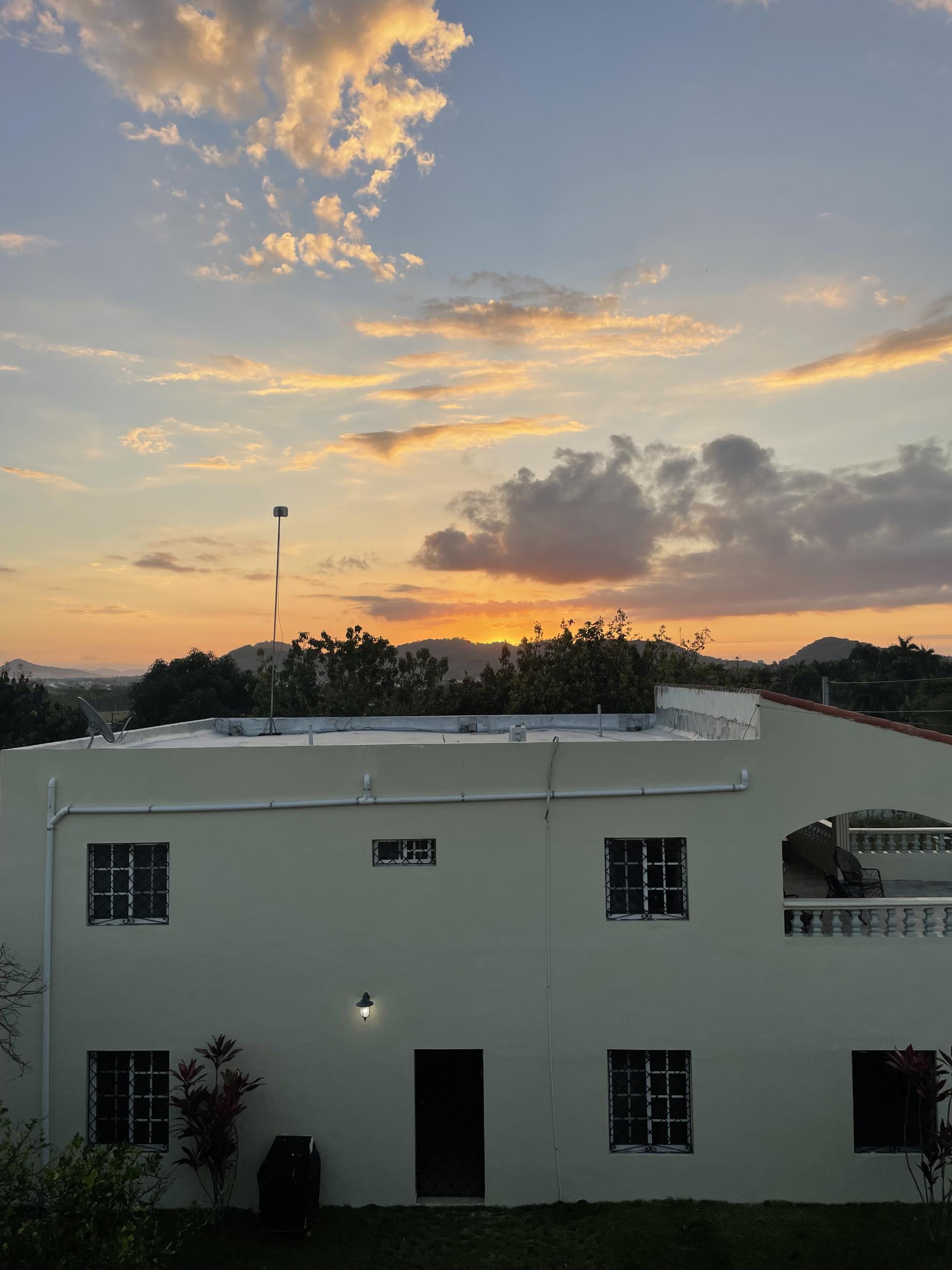 The sun set overlooking a white building with orange tinted clouds looming above. 