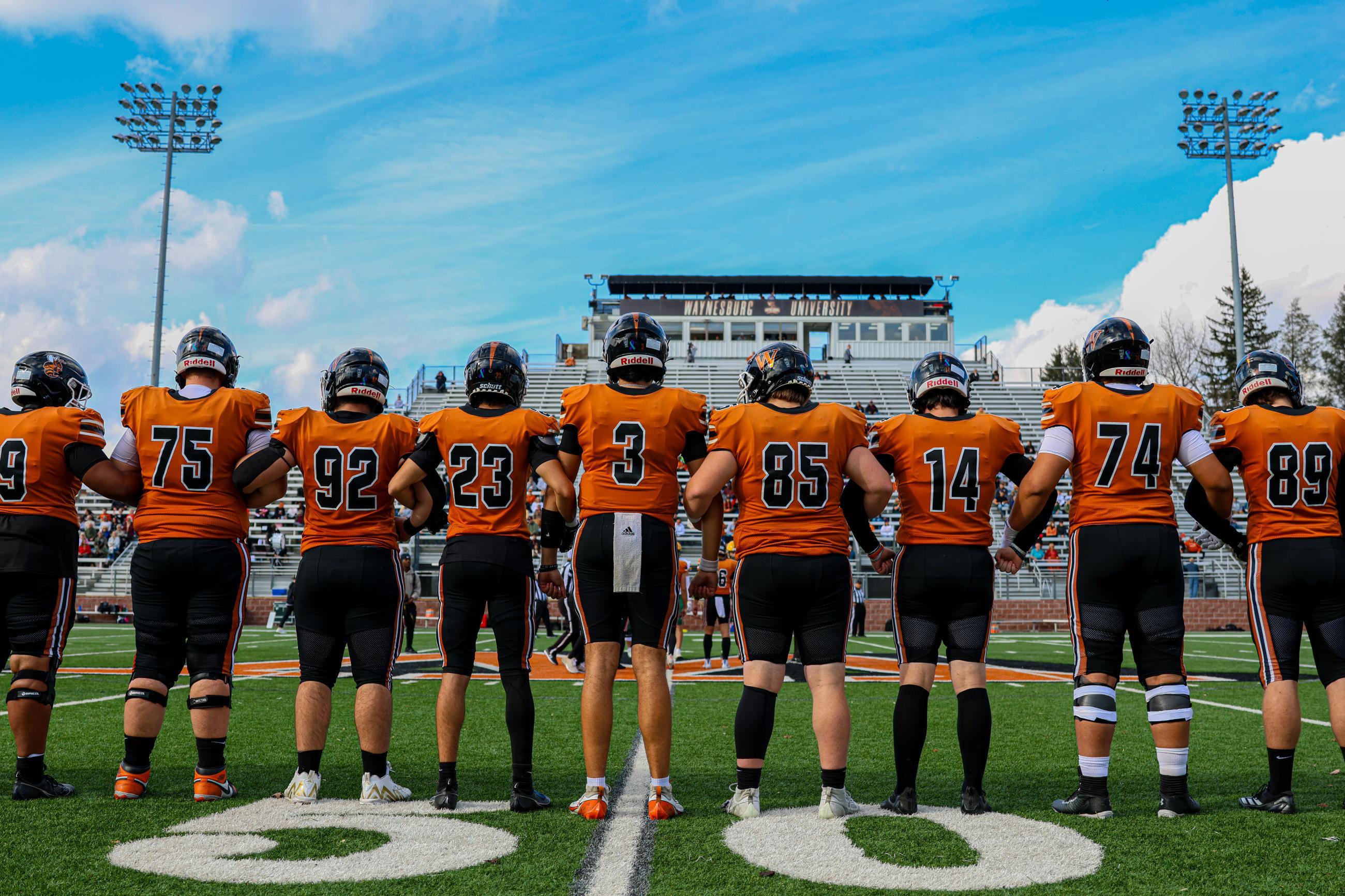 Members of the Waynesburg University football team arm in arm on the field at Wiley Stadium in fall 2025