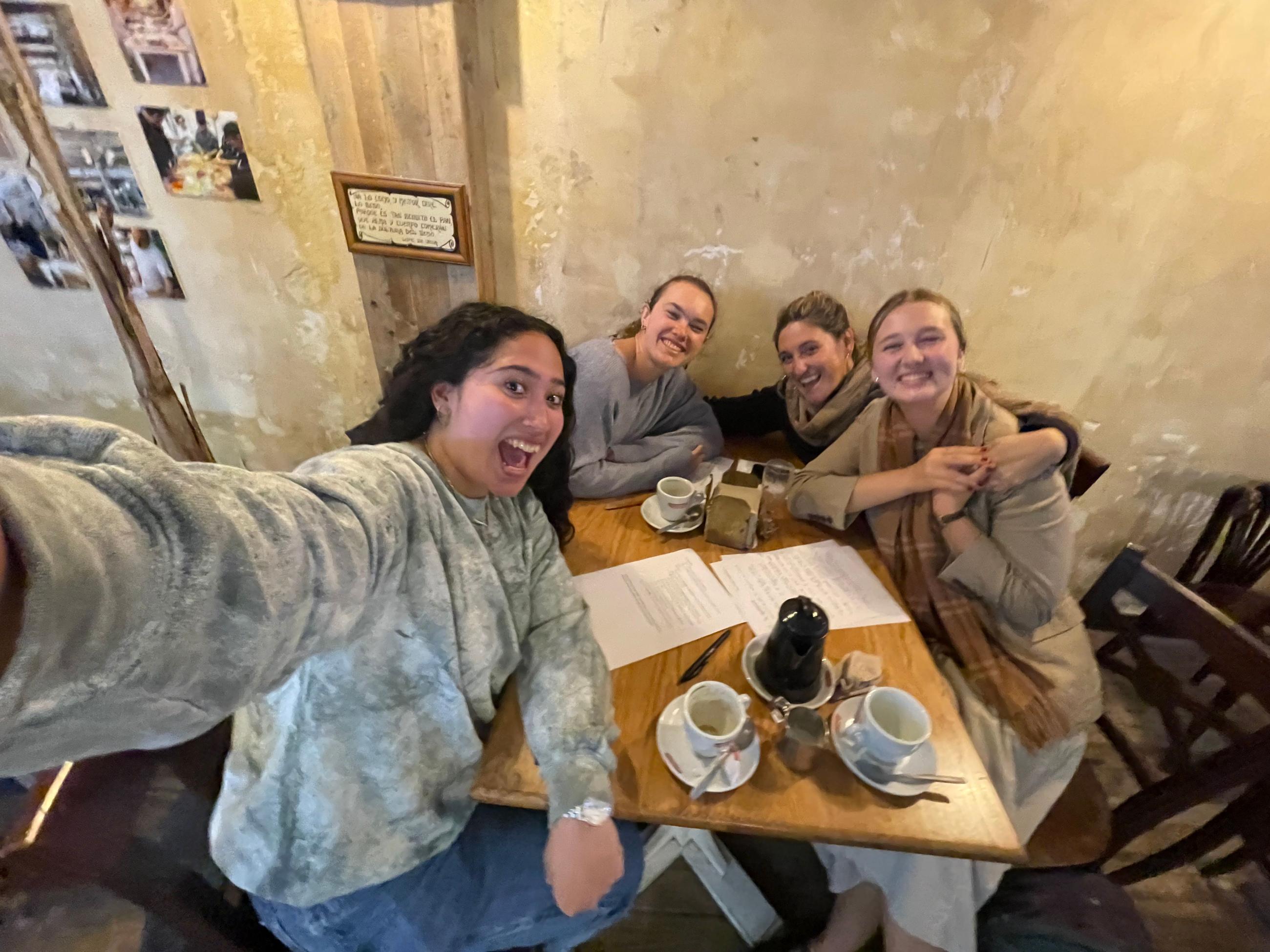 Natalie sits to the left at a table with two classmates and their teacher. 