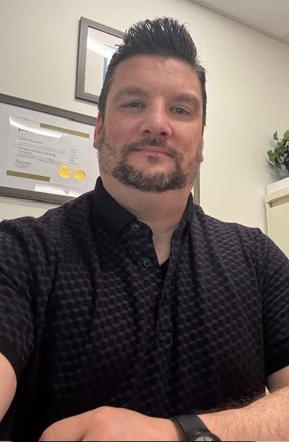 Justin Panepinto, a man with dark hair and a short beard wearing a black shirt, sits in his office