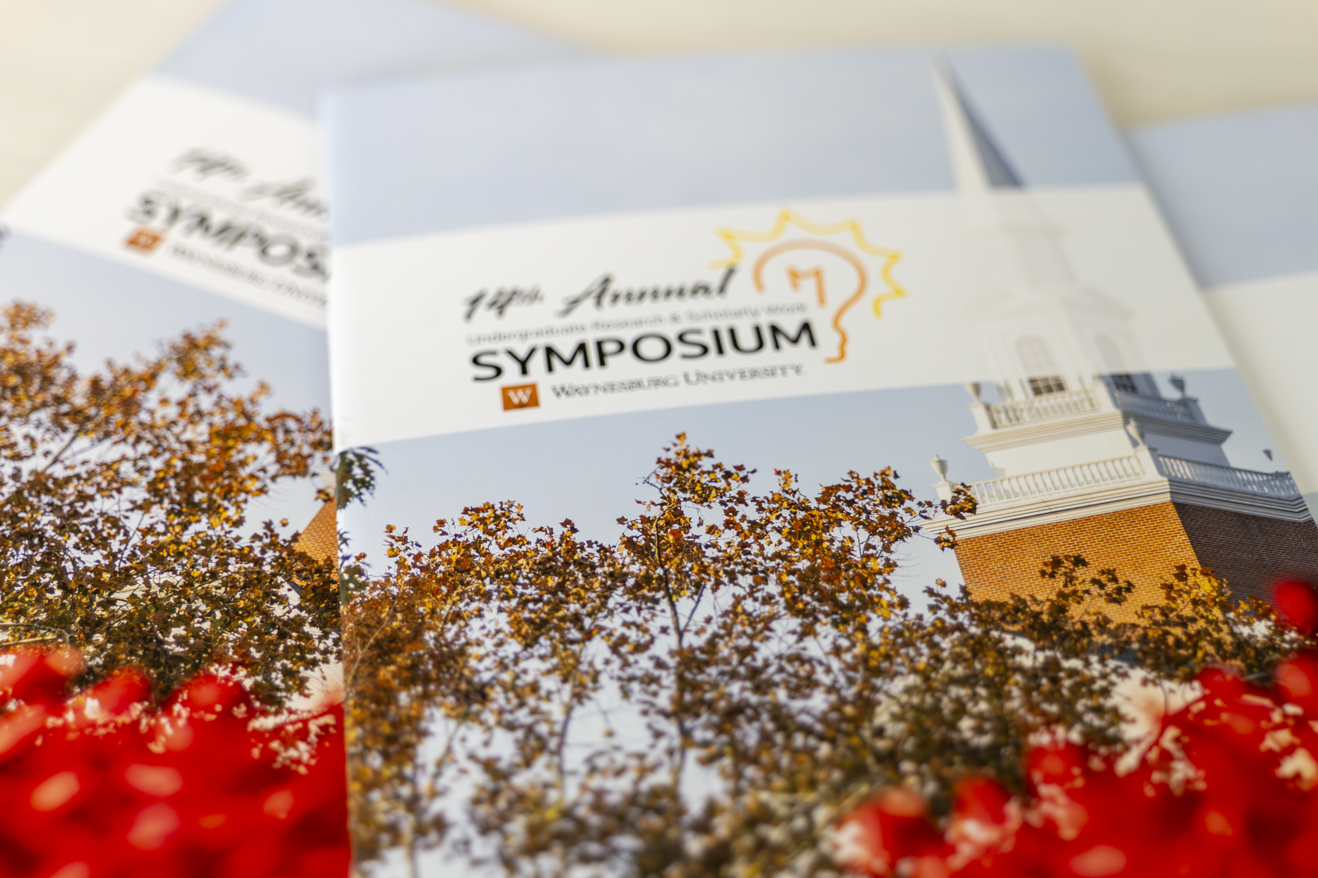 Printed programs for the 14th Annual Undergraduate Research and Scholarly Work Symposium displayed on a table