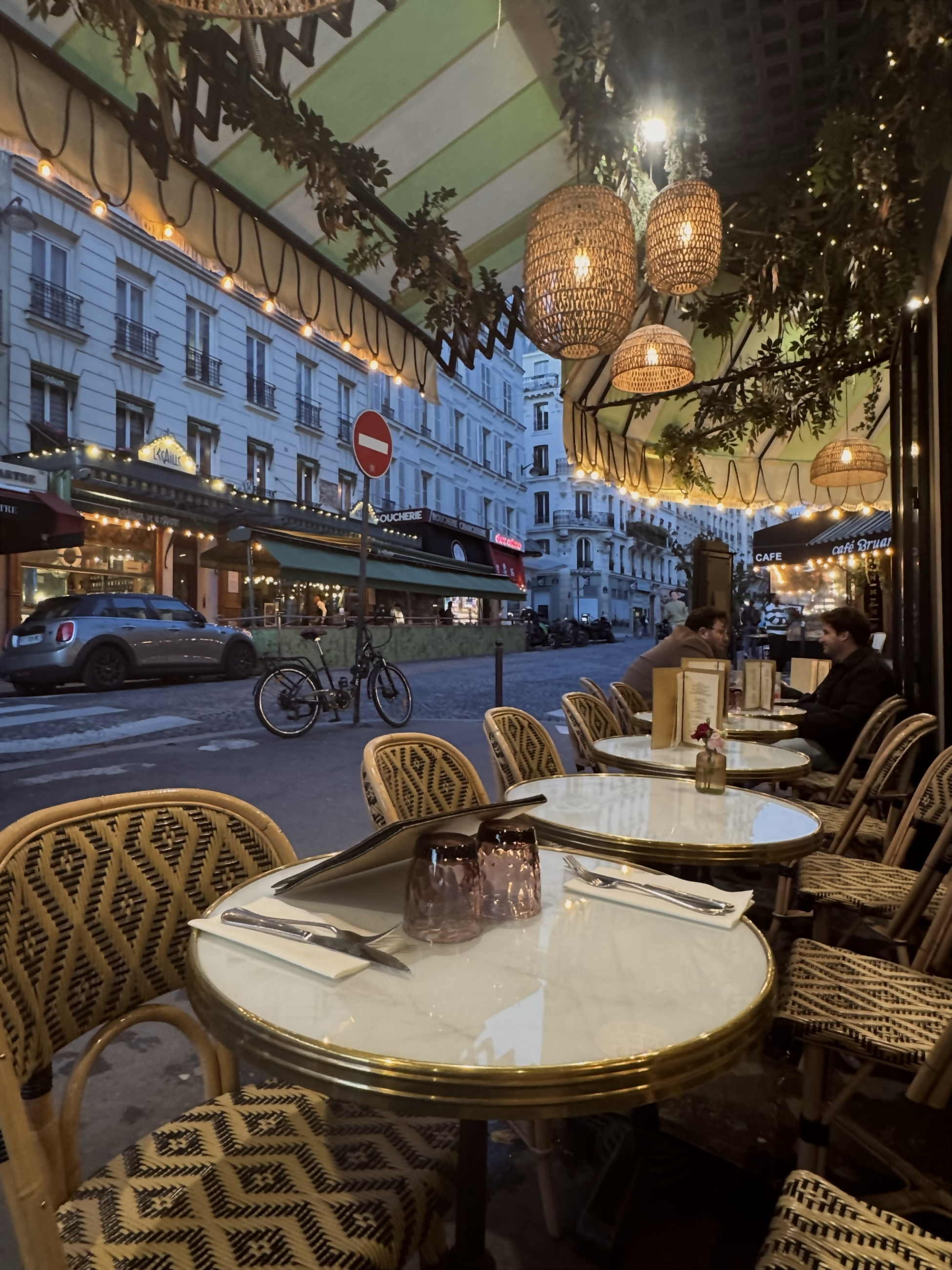 Candlelit cafe tables and chairs sit under an outside canopy on a Parisian street.