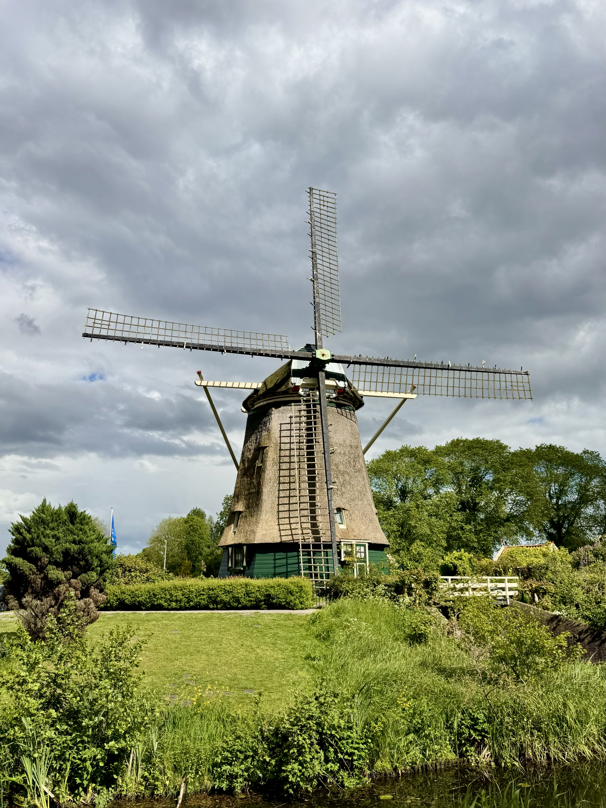 A windmill sits in a green grassy meadow with bushes