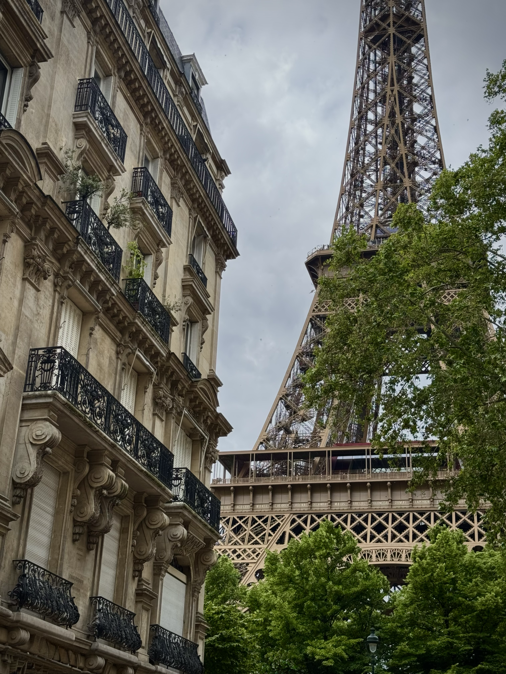 The Eiffel Tower, a tall metal industrial structure, can be seen between the buildings on a Parisian street.