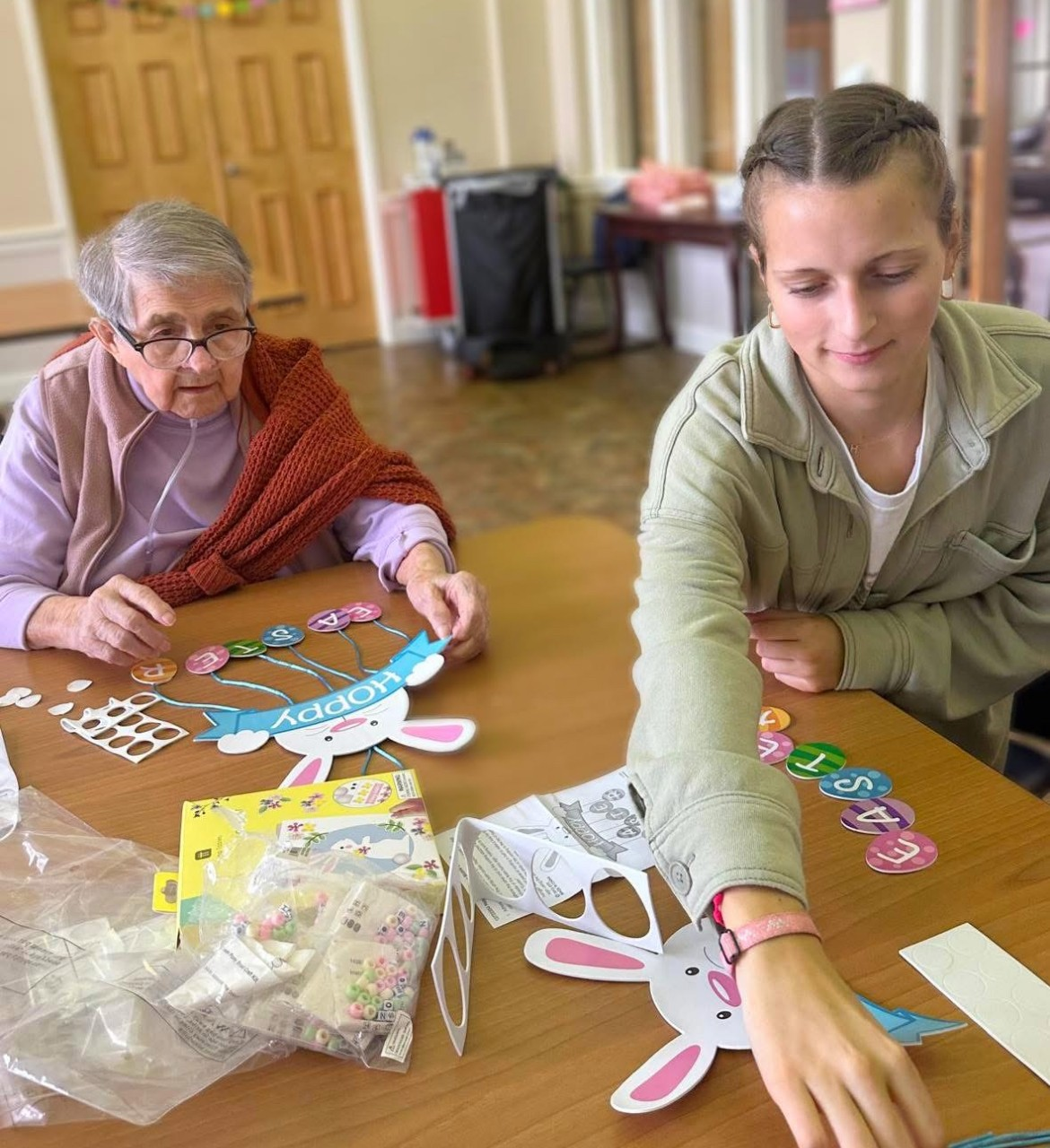 A student and elderly person make crafts together at a table.