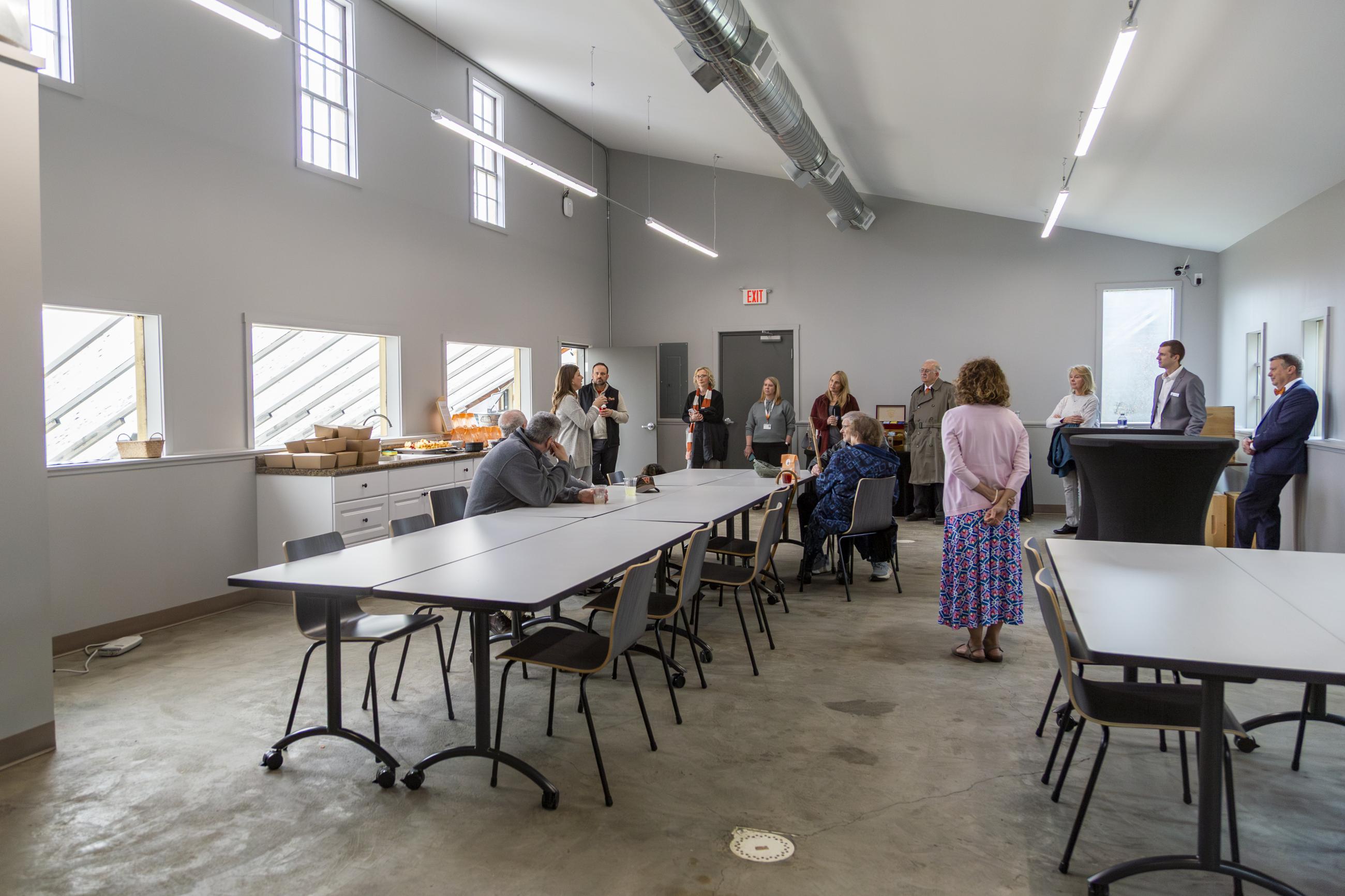 The classroom including long tables and people standing around them.