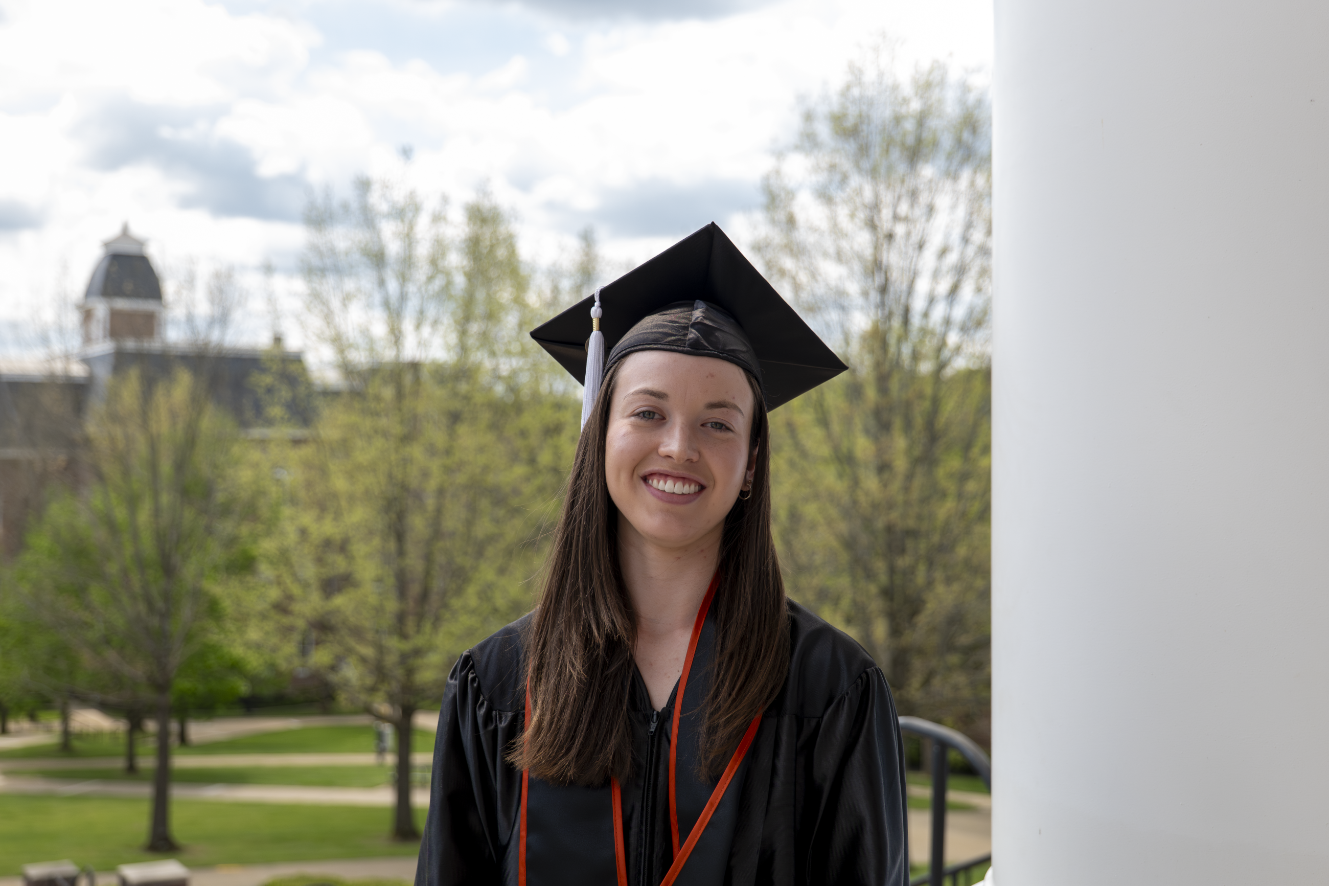 Emily Barker pictured in her cap and gown with Miller Hall in the background