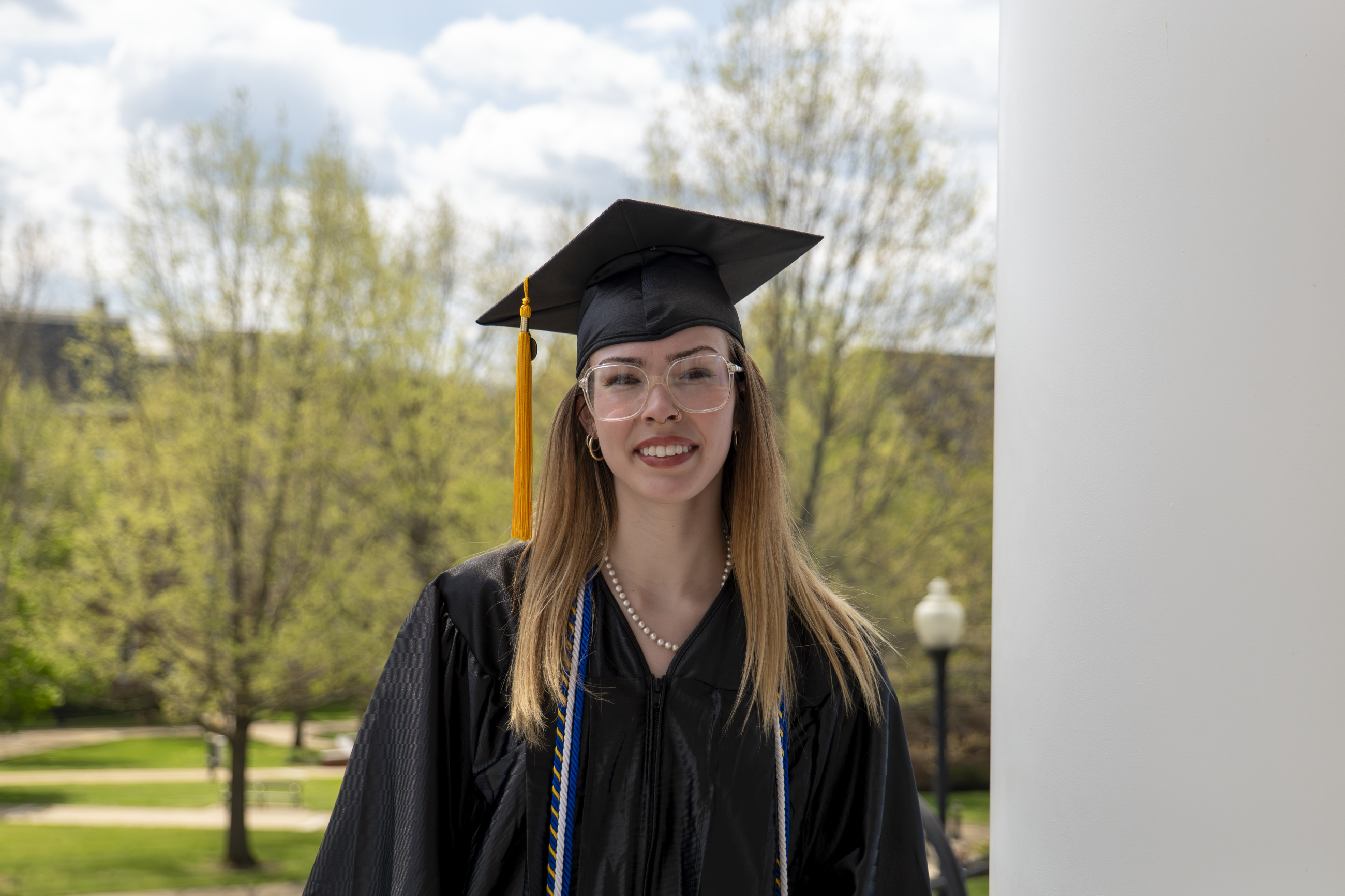 Hailey Crusenberry pictured in her graduation regalia, posing in front of the columns of Roberts Chapel on Waynesburg's campus
