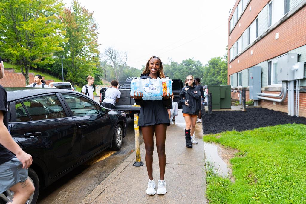 A student smiles for the camera with a package of bottled water during new student move in.