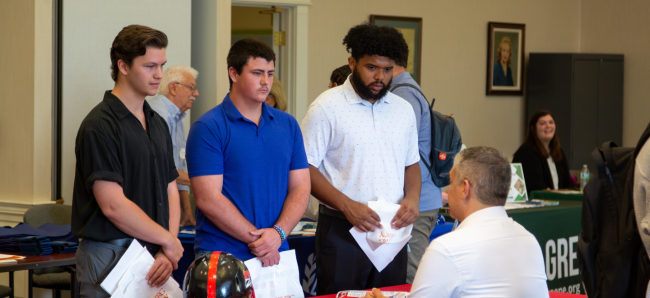 Three students at the Business & Communication Job and Internship Fair talking with an employer representative