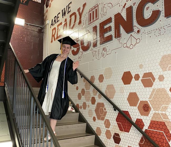 Kate James standing in a stairwell wearing academic regalia