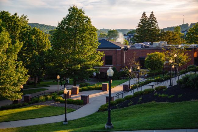 Green leafed trees surround the Benedum Dining Hall and the sun shines from the right.