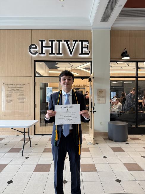 Evan Como stands in front of the Waynesburg University eHIVE with an award