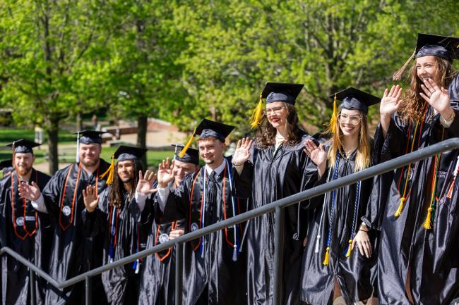 Graduates in regalia wave at the camera.