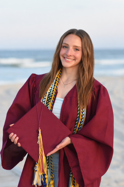 Cheyenne Haskell posing with her graduation cap and gown on the beach