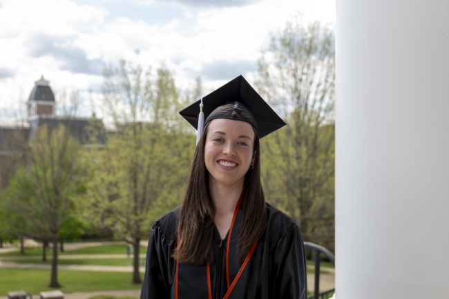 Emily Barker pictured in her cap and gown with Miller Hall in the background