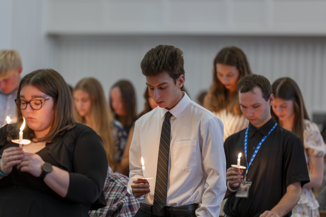 Students holding white wax candles and bowing their heads during the ALD induction candle ceremony in Roberts Chapel