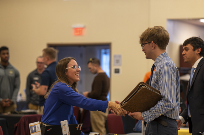 A student shaking hands with an employer at the Business & Communication Job & Internship Fair held in the Marsh Center on campus